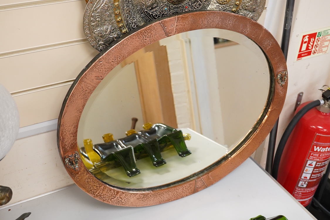 An oval late 19th century hammered copper wall mirror with rams head cartouches, 65cm wide
